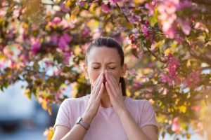 Young women stopped to sneeze as she walked by a tree during spring.