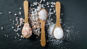 Three wooden spoons with fine salt, white salt rocks, and pink salt rocks.