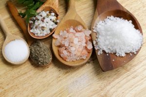 Five wooden spoons of different sizes with a variety of salts.