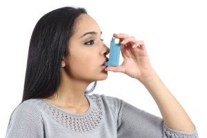 Head shot of an Indian woman using an inhaler.