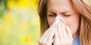 Woman sneezing into tissue while being outdoors.