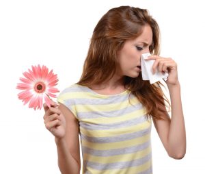 Young woman sneezing on a tissue due to a flower being held on her right hand.