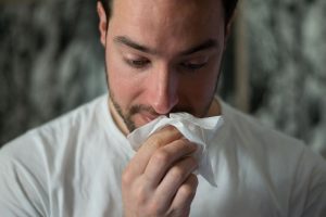 Middle aged man wiping nose with tissue.