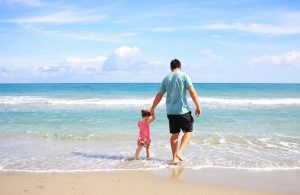 Father holding daughters hand as they walk on ocean shore.