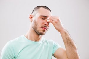 Young man with headache and sinusitis applying pressure on nose and sinus areas.